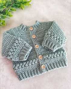 a crocheted sweater with buttons on the front and back, sitting next to a potted plant