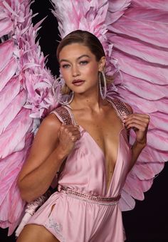 a woman in a pink dress with large feathers on her head and arms, posing for the camera