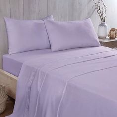 a bed with lavender colored sheets and pillows