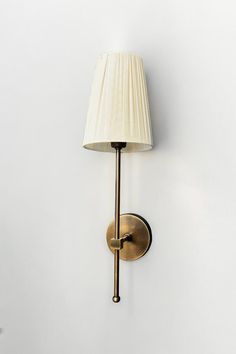 a wall light with a white shade on it's side and a lamp attached to the wall