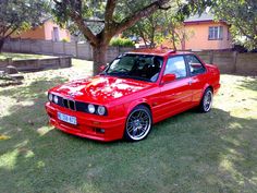 a red car parked in the grass next to a tree