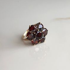 A vintage 9 carat yellow gold Garnet floral cluster ring. This beautiful piece holds a gorgeous collection of deep red stones in a gold setting. CONDITION: Good condition, wear consistent with age and use. Please see photos for more detail. HALLMARKED 9 CARAT GOLD, ASSAYED IN LONDON 1975 SETTING SIZE DIAMETER: 18mm SMALLER STONE SIZE: 6mm (.50 carat) CENTRAL STONE SIZE: 7mm (1.0 carat) BAND WIDTH: 1.5mm RING SIZE: UK: N | US: 6 3/4 WEIGHT: 3.4 grams (UUZ) Sally Brown, Red Stones, Garnet Gem, Red Band, Lovely Ring, Red Stone, Multi Stone Ring, Multi Stone, Cluster Ring