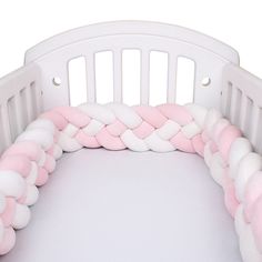 a white crib with pink and white braids on the sides, in front of a white background