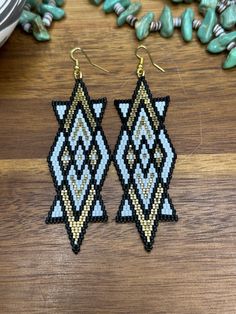 the beaded earrings are made with black, white and gold beads on a wooden surface