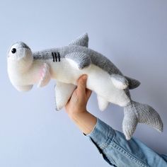 a hand holding a stuffed shark toy in the shape of a fish on a white background