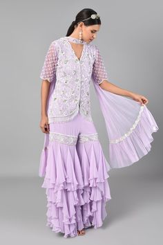 Lilac short kurta with bugle beads, pearl and sequin floral motifs. Comes with sharara and dupatta.
Component: 3
Pattern: Embroidered
Type Of Work: Bugle Beads, Pearl and Sequin
Neckline: V neck
Sleeve Type: Half
Fabric: Georgette and Net
Color: Purple
Other Details: 
Sharara with ruffle detail
Bead hangings
Dupatta with ruffle border
Sheer sleeves with scallop border
Closure: Hook front
Occasion: Sangeet - Aza Fashions Traditional Hand Embellished Purple Sets, Hand Embellished Purple Wedding Sets, Elegant Hand Embellished Purple Sets, Elegant Beaded Sets For Festive Season, Elegant Beaded Sets For Festive Occasions, Elegant Beaded Festive Sets, Elegant Purple Sharara For Celebration, Festive Beaded Party Sets, Elegant Embellished Sharara For Celebration