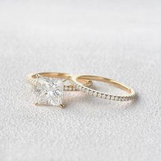 two gold wedding rings with a princess cut diamond in the center and side stones on each band