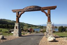 a wooden sign on the side of a road next to a body of water with mountains in the background