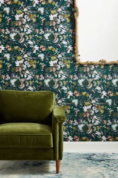 a green chair in front of a floral wallpaper with a gold framed mirror on it