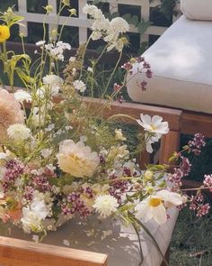 a vase filled with lots of flowers sitting on top of a wooden table next to a bench