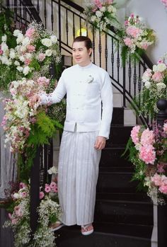 a man standing in front of flowers on the stairs with his hands behind his back