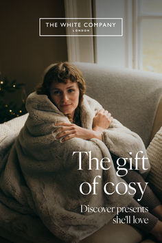 a woman wrapped in a blanket sitting on a couch with the words, the gift of cosy