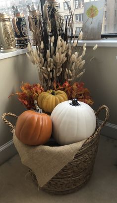 a basket filled with pumpkins and gourds on top of a floor next to a window