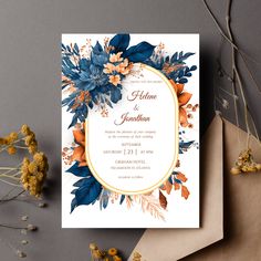 a wedding card with blue and orange flowers on it, next to some dried flowers