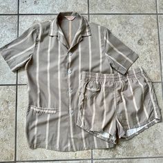 Here is a vintage cabana set by "Palmland Fashions," that can be dated to the 1960s. The set is tagged a size Small, but please use the measurements provided to ensure a proper fit. Made of what is assuredly 100% cotton, it has a taupe background and a lightly textured beige stripe on both the top and trunks.  The shirt features a camp collar, short sleeves, and hip pocket with terry cloth piping; the trunks have an elastic waistband & drawstring closure, a flapped change pocket on the right hip Taupe Background, Ivy League, Mens Swim Trunks, Swimwear Fashion, Terry Cloth, Swim Trunks, Button Up Shirts, 1960s, Short Sleeves