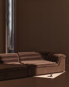 a brown couch sitting in front of a window next to a lamp on a table