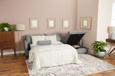 a bedroom with pink walls and white bedding has a gray couch in the corner