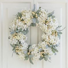 a wreath with white flowers and greenery hangs on the front door