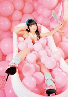 a woman sitting in a bathtub surrounded by pink balloons