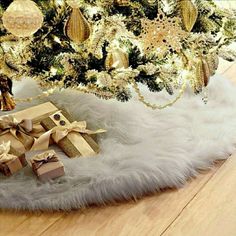 a christmas tree with presents under it in front of a white fur covered tablecloth