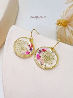 the dandelion earrings are on display next to a flower vase with flowers in it