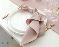 a white plate topped with a pink napkin next to a wine glass and gold utensils