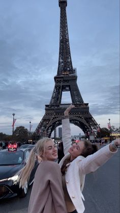 two women taking a selfie in front of the eiffel tower at dusk