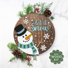 a wooden sign that says let it snow with a snowman and pine cones around it