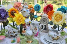 a table topped with lots of colorful flowers next to plates and vases on top of a table