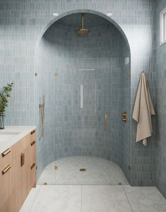 a bathroom with blue tile and gold fixtures, including a shower head in the corner