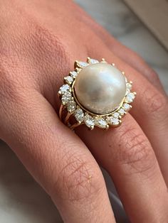 "Vintage pearl and diamond ring set in 18 karat solid yellow gold. The pearl is set with over 3 carats in marquise and round-cut diamond halo. This South Sea Pearl bears a vibrant white luster with little to no blemishes. The perfect heirloom piece that echoes a statement of refined class and taste. Polished finish for extra brilliance and shine. Certificate of appraisal included upon request. Ring Details: ✔ Ring Size: 7.5 U.S. (adjustable) ✔ Ring Weight: 20.3 grams ✔ Gold Purity: 18K Pearl Det Pearl Rings In Gold Vintage, Cocktail Ring Aesthetic, Luxury Formal Pearl Ring With Halo Design, Luxury Brilliant Cut Pearl Ring For Wedding, Formal Yellow Gold Pearl Ring With High Luster, Formal 14k Gold Pearl Ring With 17 Jewels, Formal High Luster Yellow Gold Pearl Ring, Brilliant Cut Pearl Ring Fine Jewelry, Fine Jewelry Pearl Ring With Brilliant Cut