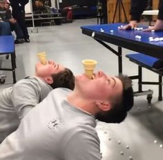 two people laying on the ground with cups in their mouths and one person holding an ice cream cone above his head