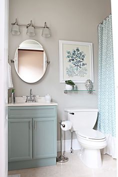 a white toilet sitting next to a sink in a bathroom under a round mirror on the wall