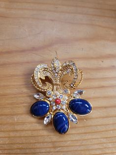 The brooch is a fleur di lis design with 15 carats created blue sapphire cabochans with a 1mm red ruby cabochan and .5mm white crystal accents.  18K gold plated. Ruby Bracelet, Cameo Necklace, Real Stone, Genoa, Red Ruby, White Crystal, Floral Earrings, Locket Necklace, Beautiful Earrings