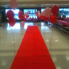 a long red carpeted hallway with balloons on the floor and tables in the background