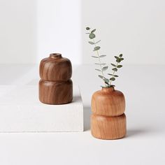 two wooden vases with plants in them on a white surface, one is made out of concrete