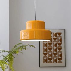 an orange lamp hanging from a ceiling in a room with plants and pictures on the wall