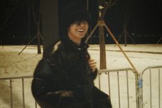 a woman standing in front of a metal fence at night with snow on the ground