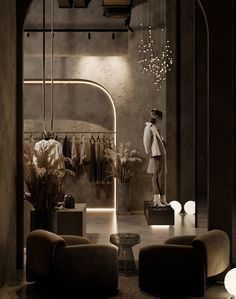 a woman standing in front of a clothing rack with clothes hanging on the wall and two chairs