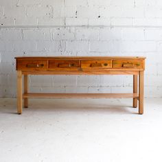 an old wooden table with two drawers on one side, against a white brick wall