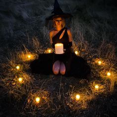 a woman sitting on the ground with candles in her lap and wearing a witches hat