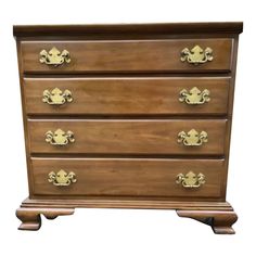 a wooden dresser with four drawers and gold handles on it's sides, isolated against a white background