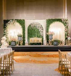 an indoor wedding setup with white flowers and greenery on the wall, gold chairs and candles