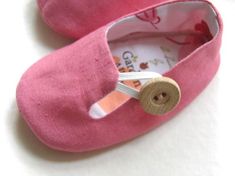 a pair of pink baby shoes with a wooden button