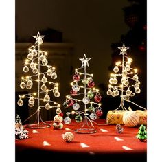 three small christmas trees on a table with lights and ornaments around them in front of a black background