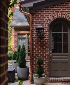 a brick house with two potted plants and a lamp on the front door way