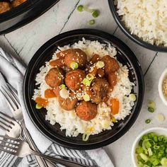 meatballs and rice are served in black bowls on a white table with silverware