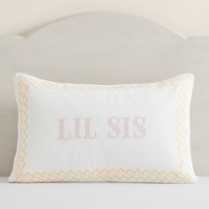 a white pillow with the word lil sis on it in pink and yellow embroidered across the front