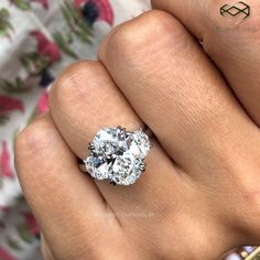 a woman's hand with a diamond ring on top of her finger and the other hand holding an engagement ring