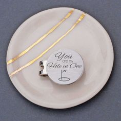 a white plate topped with two pieces of silverware and a small round pendant that says, you are my hole in one